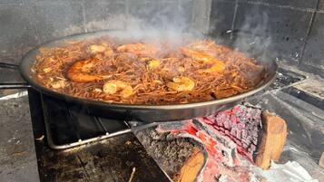 A large pan filled with a seafood dish over an open flame.