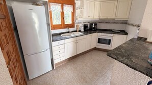 A kitchen with white cabinets, a refrigerator, a sink, a stove, and a window with lace curtains.