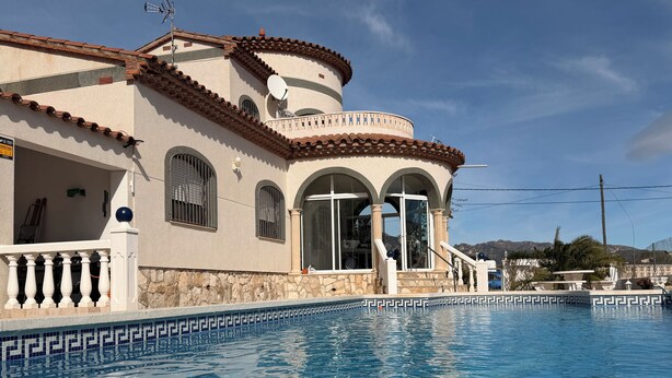 A poolside view of a building with a pool, a balcony, and a mountain backdrop.