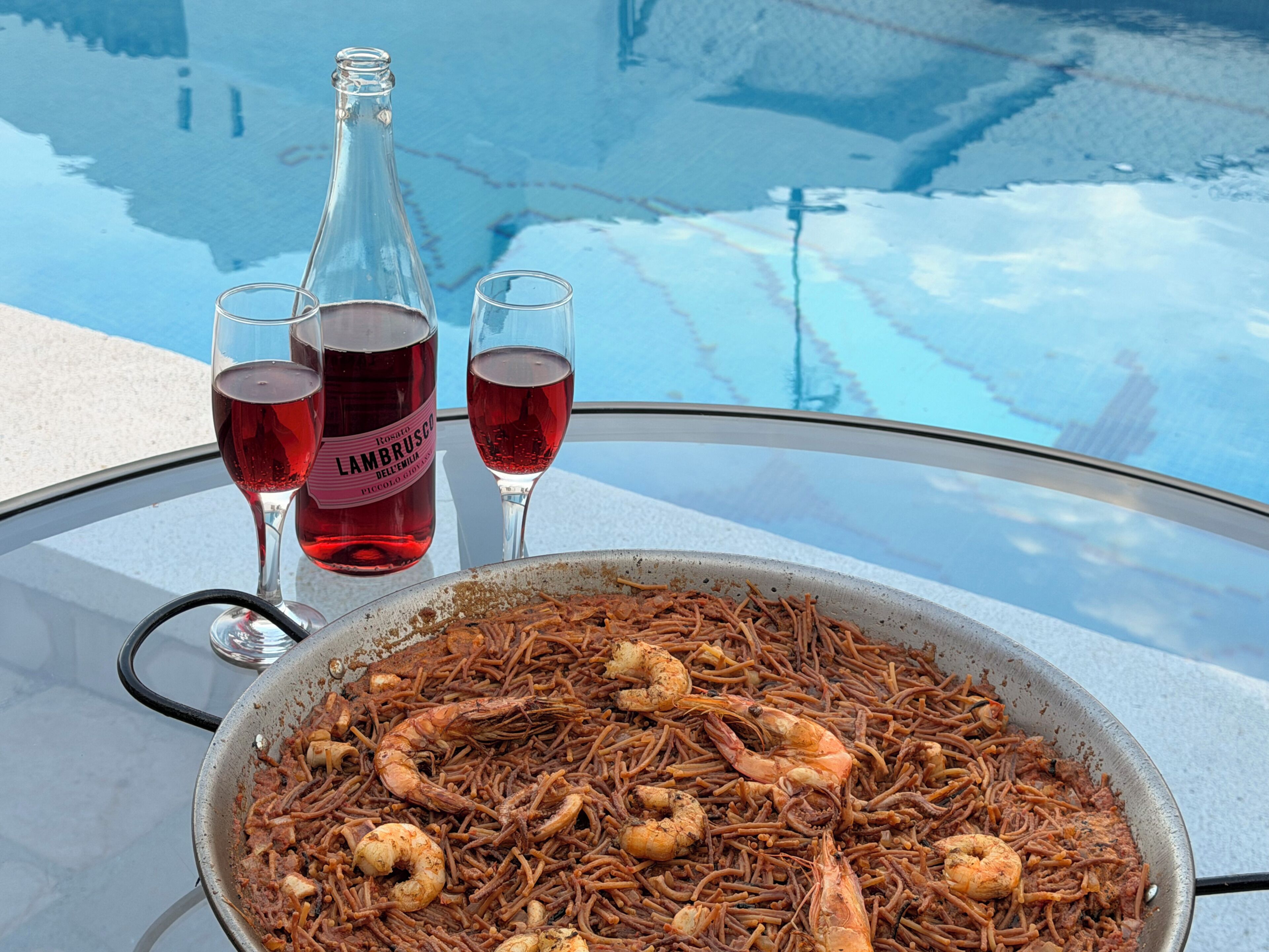 Un plat de fruits de mer est servi sur une table, accompagné d’une bouteille et de verres de vin rouge.