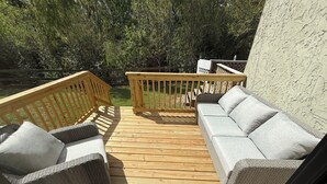 Eine Holzterrasse mit einer Couch und Stühlen, einem kleinen Tisch und Blick auf einen Garten.