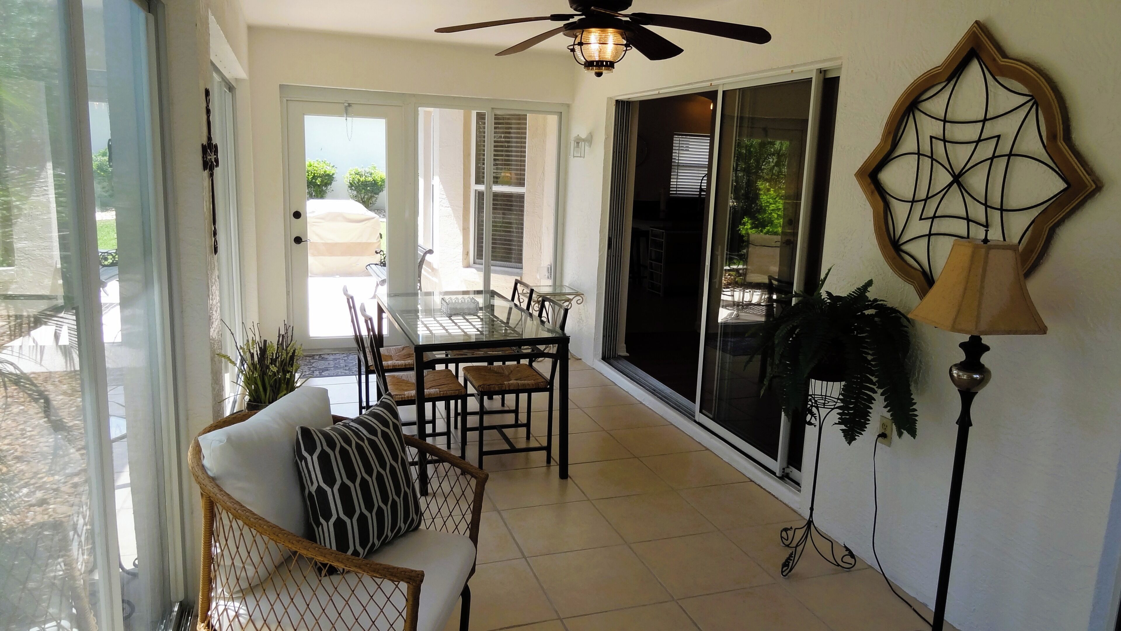 A dining area with a glass table and chairs, a ceiling fan, and a decorative wall piece.