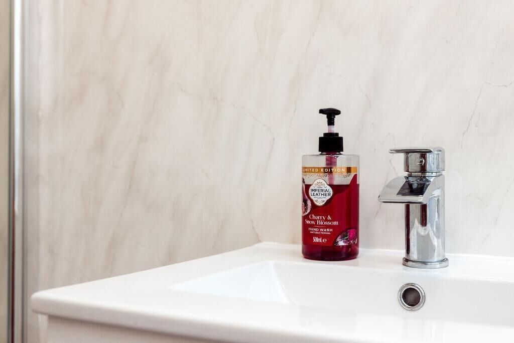 A bathroom with a white sink, a chrome faucet, and a bottle of hand soap.