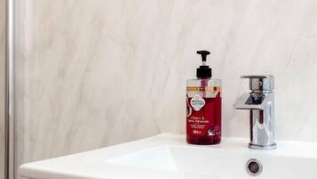 A bathroom with a white sink, a chrome faucet, and a bottle of hand soap.