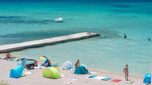 Ein Strand mit Zelten, einem Steg und klarem türkisblauem Wasser.