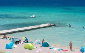 Una playa con tiendas de campaña, un muelle y agua turquesa cristalina.