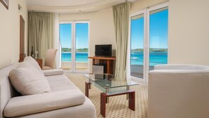 A hotel room with a sofa, a glass coffee table, a TV, and a view of the sea through large windows. - Hotel Duje (Vodice)