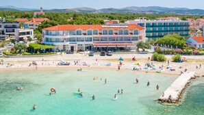 A coastal hotel with multiple floors, a beach in front, and a clear view of the sea. - Hotel Duje (Vodice)