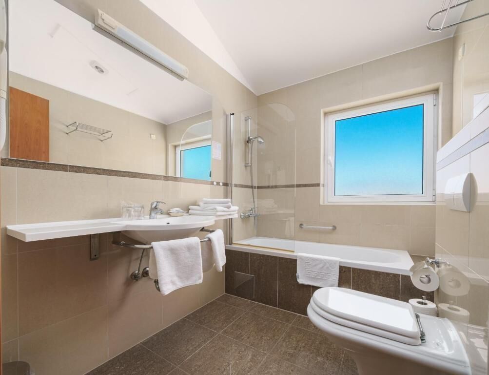 Une salle de bain moderne avec une douche à parois de verre, une grande fenêtre, un lavabo blanc et des toilettes.