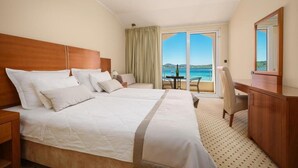 A hotel room with a large bed, a desk, a chair, and a view of the sea. - Hotel Duje (Vodice)