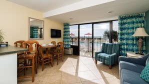 A room with a dining table, chairs, a sofa, a TV, and a balcony with umbrellas. - Perfect 2-bedroom apartment with AC in North Myrtle Beach peppertree (North Myrtle Beach)