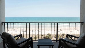 Ein Balkon mit Blick auf einen Strand, zwei Stühle und ein kleiner Tisch.