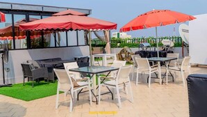 Een terras buiten met tafels en stoelen, rode parasols en een schotelantenne.