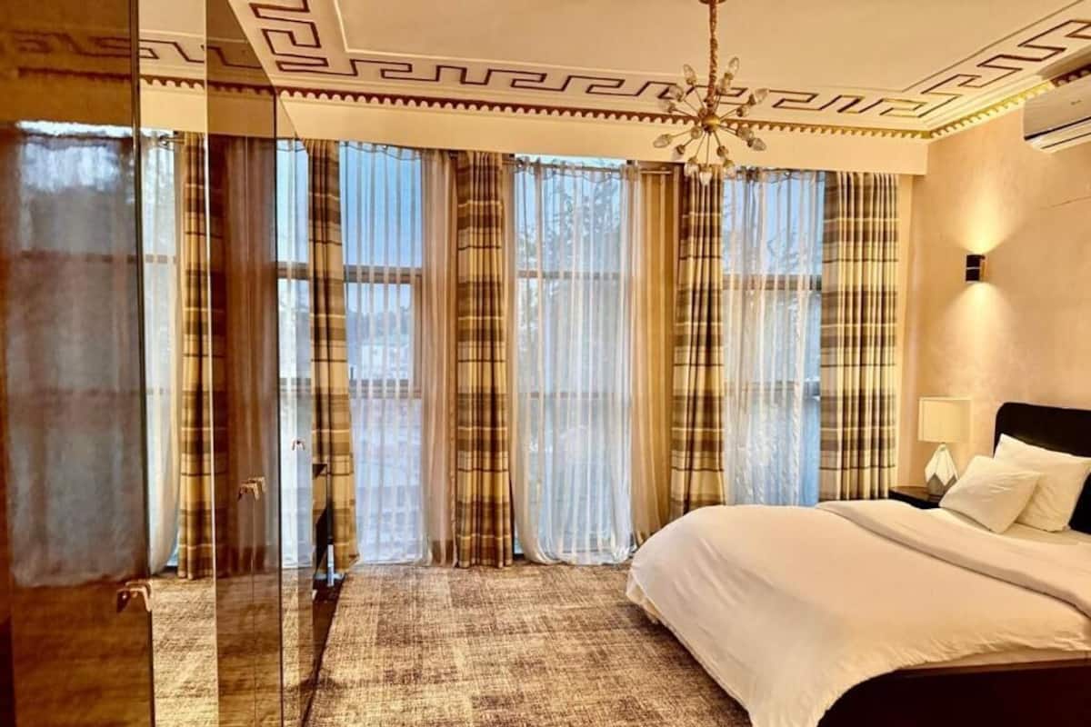 Ein Hotelzimmer mit einem großen Bett, einer Kronleuchter und Blick durch leichte Vorhänge.