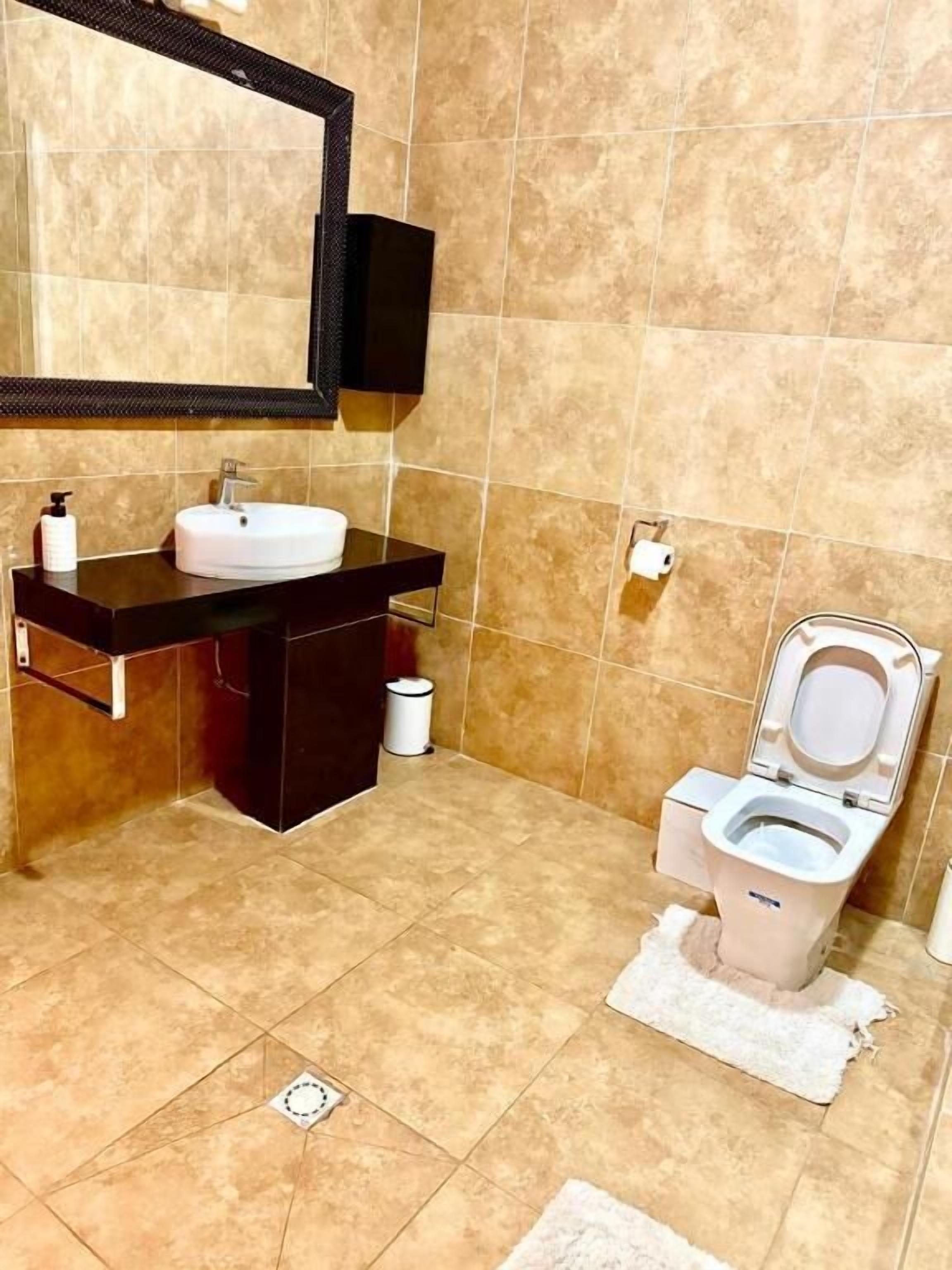 Een badkamer met een wastafel, spiegel, toilet en een prullenbak.