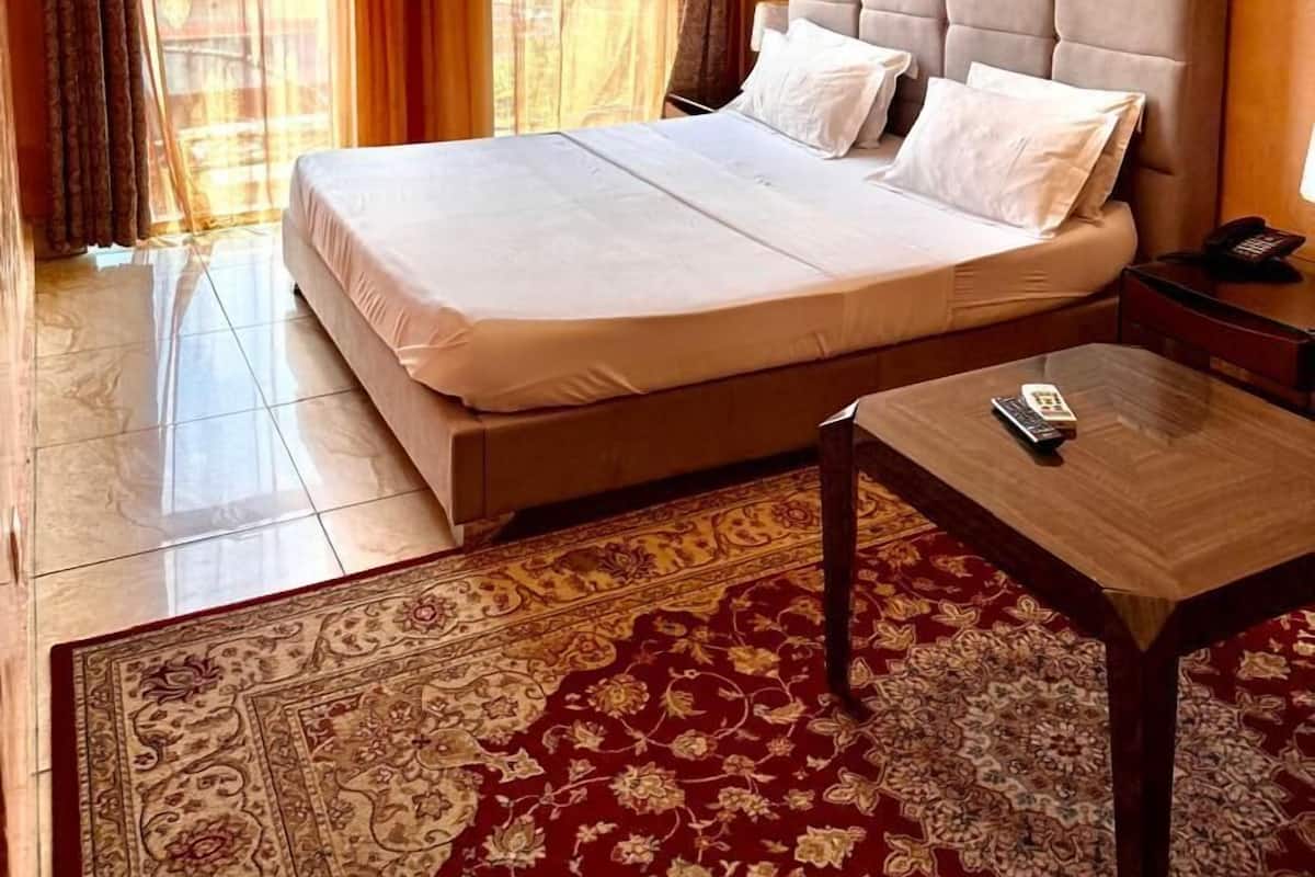 Ein Hotelzimmer mit einem großen Bett, einem Fernseher, einem Schreibtisch mit Fernbedienung und einem gemusterten Teppich.