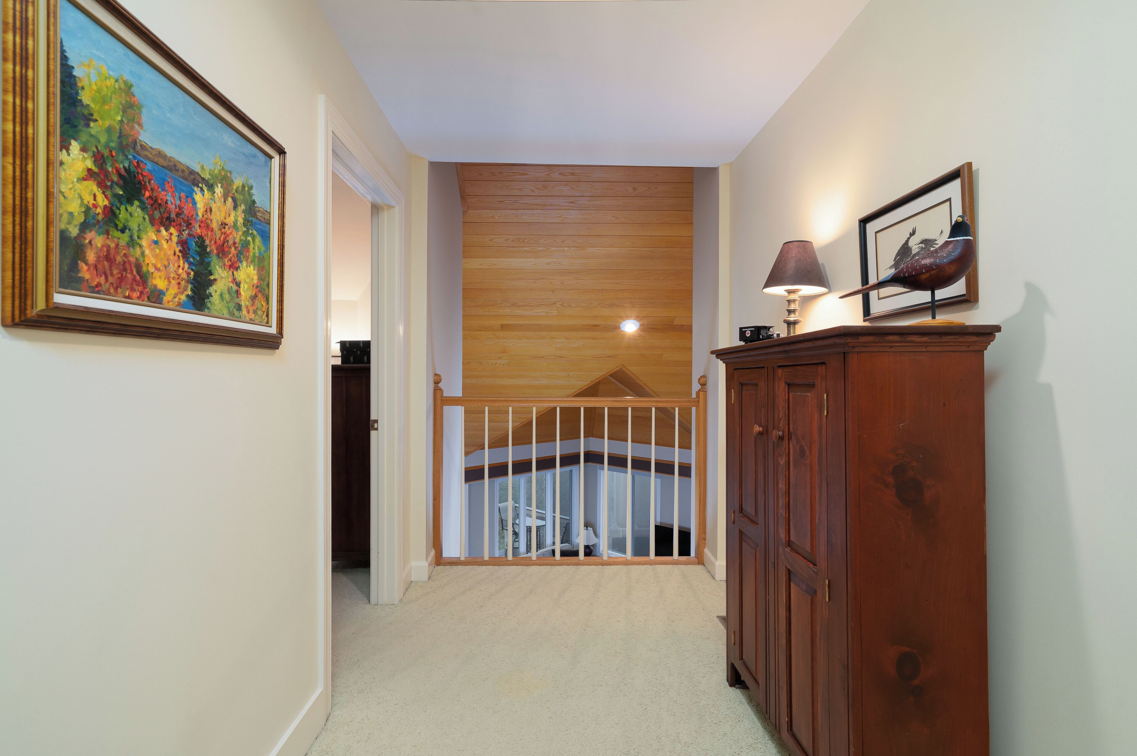 A hallway with a wooden ceiling, a painting on the left, a lamp on the right, and a wooden cabinet.