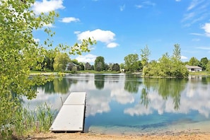 Un lac paisible, avec une jetée qui s’avance sur l’eau, entouré de verdure et d’arbres.