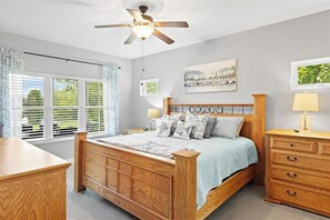 Une chambre à coucher avec un lit en bois, un ventilateur de plafond, une fenêtre avec des stores et une table de chevet avec une lampe.
