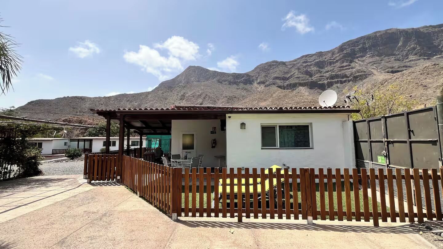 A small building with a patio, a fenced area, and a mountain in the background.