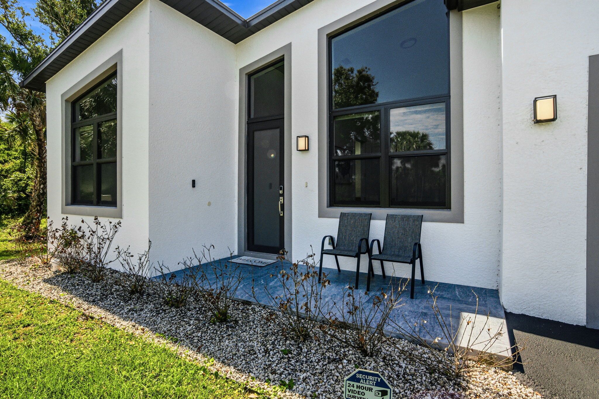 A modern house with a large window, a door, and two chairs outside.