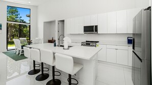 A modern kitchen with white cabinetry, a central island with bar stools, a microwave, and a refrigerator. - Christian Nature Haven (Naples)