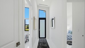 A narrow hallway with a black carpet, white walls, and a door leading to a bedroom with a bed. - Christian Nature Haven (Naples)