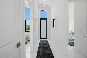 A narrow hallway with a black carpet, white walls, and a door leading to a bedroom with a bed. - Christian Haven in Nature (Naples)