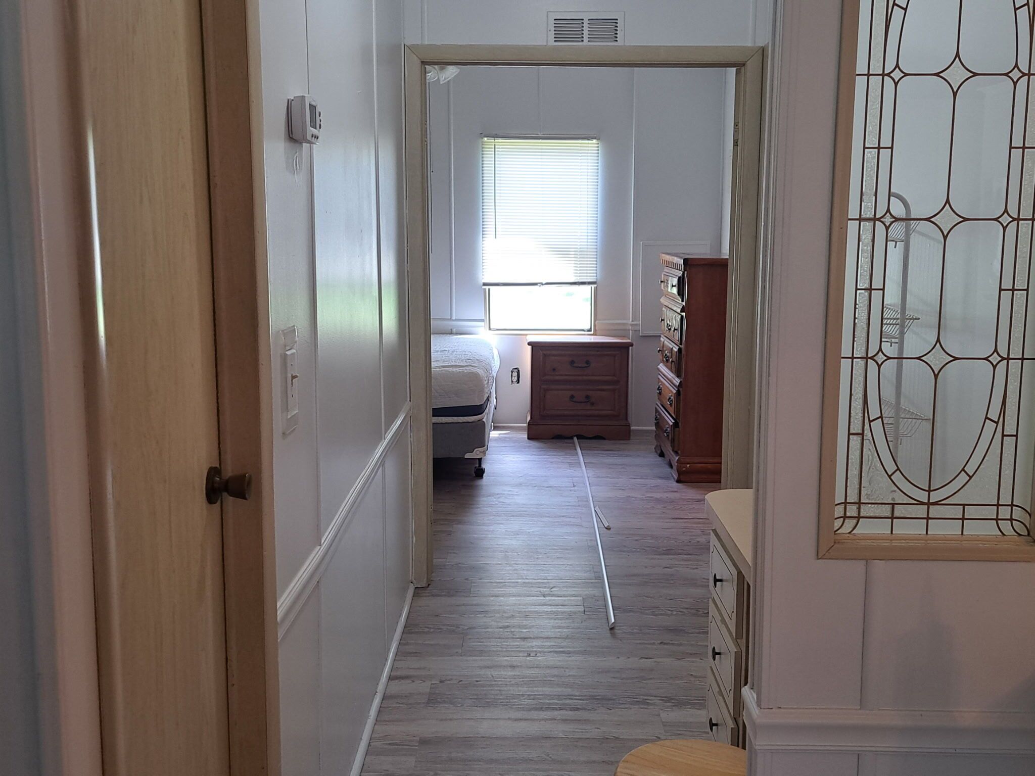 Ein schmales Dielenflur mit Bett, Schminktisch und Fenster mit Jalousien.
