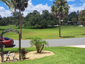 A residential area with a red car parked near a decorative metal archway, palm trees, and a well-maintained lawn. - 2-bedroom house in Silver Lake / Spanish Springs inside The Villages (Lady Lake)