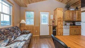 A cozy cabin interior with a sofa, wooden cabinets, a stove, and large windows.