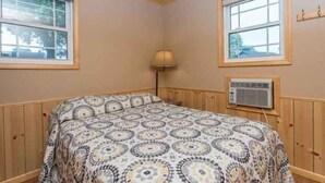 A bedroom with a bed, two windows, a lamp, and an air conditioning unit.