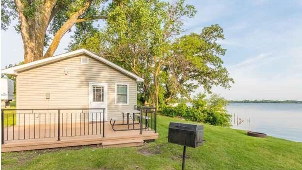A single-story cabin with a deck, a mailbox, and a lake view.