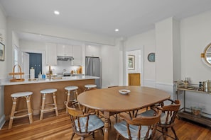 A modern kitchen with white cabinets, a central island, and a dining area with a wooden table and chairs. - Mystic Family Home 5-Min Walk to Mystic Seaport (Stonington)