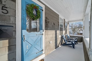 Eine Veranda mit einer blauen Tür, einem Briefkasten und drei Adirondack-Stühlen.