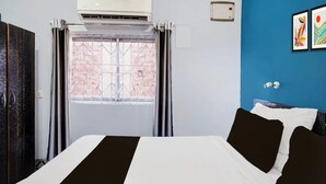 A hotel room with a bed, an air conditioning unit, a window with metal bars, a blue wall, and two framed artworks. - Hotel O Noonmati Guwahati (Guwahati)