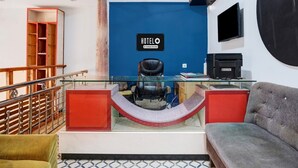 A hotel room with a blue accent wall, a black leather chair, a sofa, a glass desk, a ceiling fan, and a TV. - Hotel O Noonmati Guwahati (Guwahati)