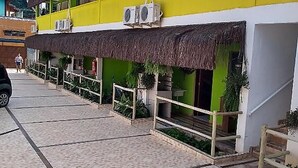 Un immeuble à plusieurs étages, doté d’une façade jaune et verte, d’un toit de chaume et d’un trottoir dallé.