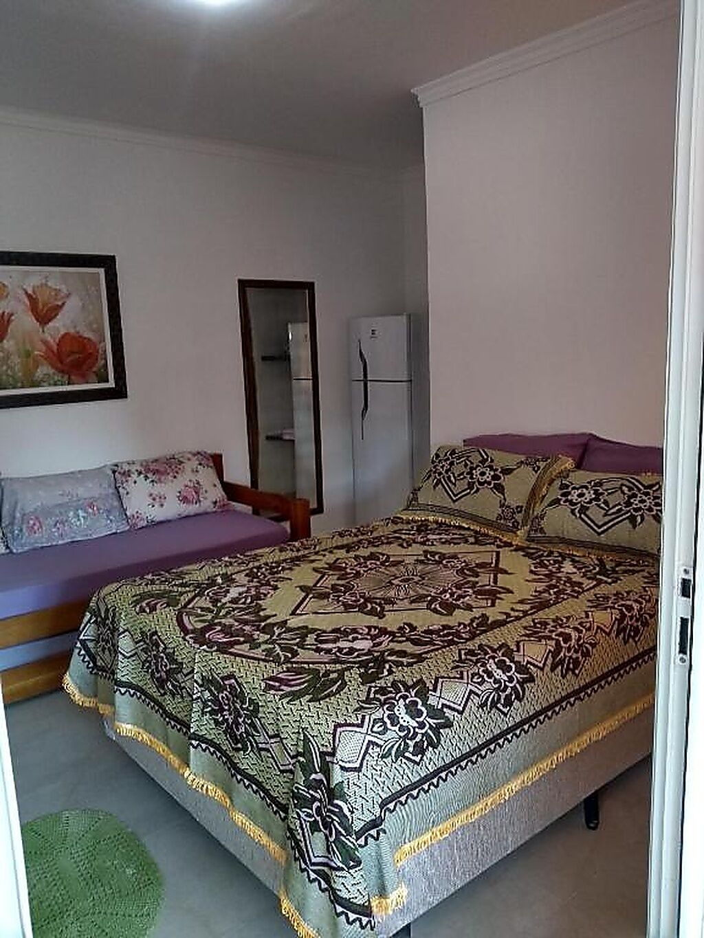 Une chambre à coucher comprenant un lit, une commode, un miroir et un réfrigérateur.