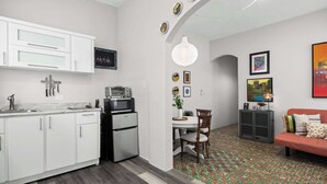 Una cocina moderna con armarios blancos, microondas integrado y refrigerador. Hay un comedor con mesa y sillas, y un sofá en la sala de estar.