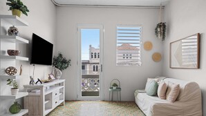 Una habitación con un sofá blanco, un televisor, estanterías con objetos decorativos, una mesita con una planta y un suelo estampado.