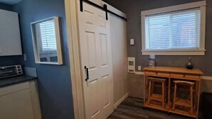 A kitchen with a white door, a wooden counter, a window with blinds, and a wall-mounted mirror. - Cozy Private Guest Suite Near SkyTrain (New Westminster)