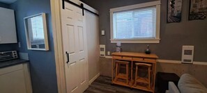 Une cuisine avec une porte blanche, un comptoir en bois, une fenêtre avec des stores et un miroir fixé au mur.