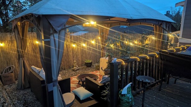 A covered outdoor seating area with string lights, wicker furniture, and a small Buddha statue. - Cozy Private Guest Suite Near SkyTrain (New Westminster)