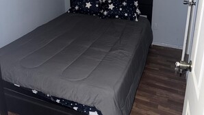 Ein Schlafzimmer mit einem Bett, einem Fenster mit Jalousien, einer Tür und einer Deckenleuchte.