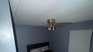 Ein Schlafzimmer mit Bett, Deckenventilator, Fenster und Tür.