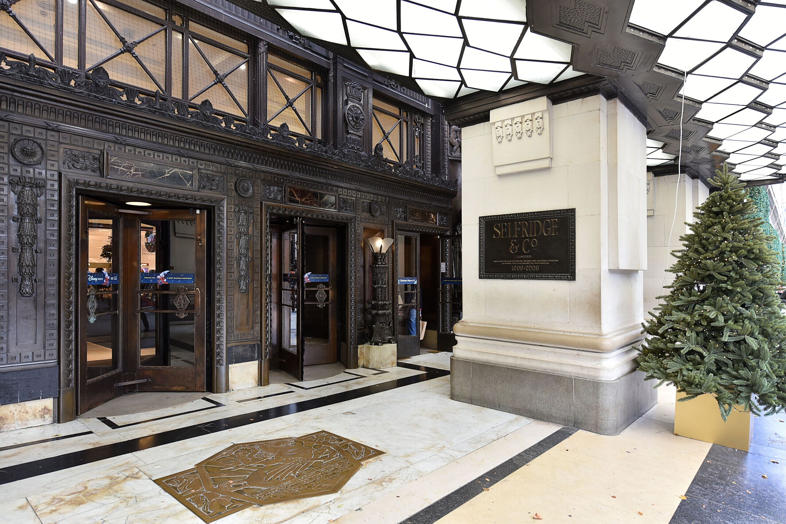 An ornate building entrance with a plaque reading "SELFAGE & CO." and a Christmas tree.