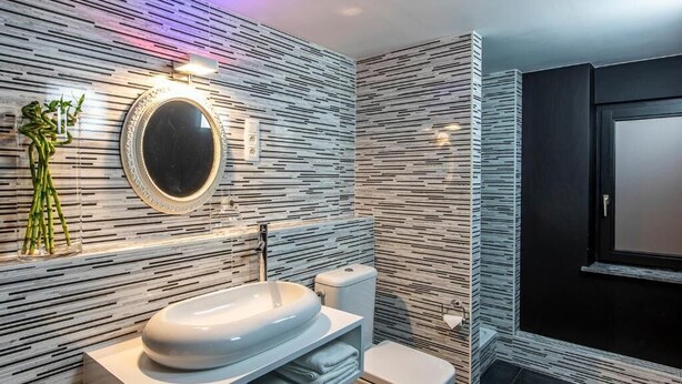 Ein modernes Badezimmer mit einem weißen Waschbecken, einem runden Spiegel und einer Toilette.
