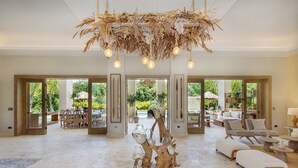 Een ruime woonkamer met een centraal geplaatst houten sculptuur, een eetgedeelte met natuurlijk licht en uitzicht op de omgeving.