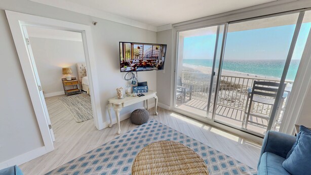 A spacious living room with a large window offering a beach view, a flat-screen TV mounted on the wall, and a comfortable seating area. - Beautiful Destin on the Gulf 506 w/Beach Service (Destin)